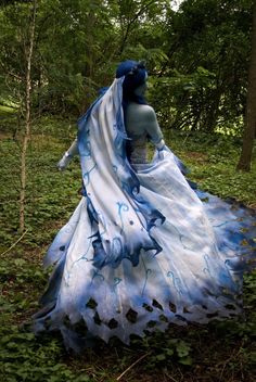 a woman in a blue and white dress walking through the woods