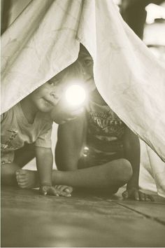 two children are playing under a tent with their flashlights on the floor in front of them