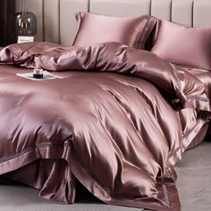 a bed with pink satin sheets and pillows