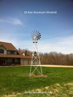 a windmill sitting in the middle of a grass covered field next to a large house