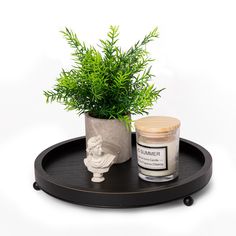 a potted plant sitting next to a candle on a black tray with a wooden lid