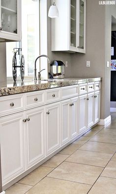 a kitchen with white cabinets and marble counter tops