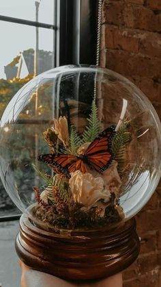 a hand holding a glass ball with flowers inside it and a butterfly in the center