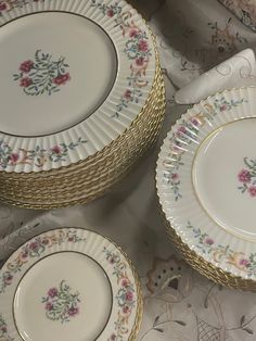 four white and gold plates with flowers on them sitting on a tablecloth covered table