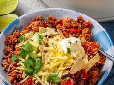 a bowl filled with taco salad and tortilla chips next to limes