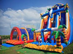 an inflatable water slide with palm trees on it and people standing near by