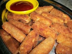 some fried food is on a plate with ketchup and mustard in the bowl