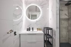 a bathroom with white marble walls and flooring, two round mirrors above the sink