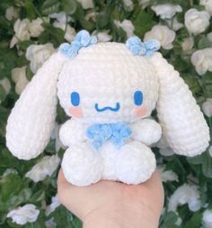 a small white stuffed animal sitting on top of a person's hand in front of flowers