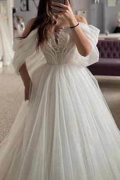 a woman taking a selfie wearing a white wedding dress with off the shoulder sleeves