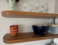 two wooden shelves with bowls and wine glasses on them in a white tiled kitchen area