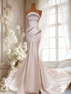 a white wedding dress on display in front of a window with flowers and curtains behind it