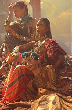 three women dressed in ethnic clothing sitting on the ground with their arms around each other