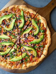 a pizza with avocado slices on it sitting on top of a wooden cutting board