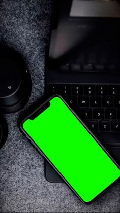 a cell phone with a green screen next to a black keyboard and mouse on a table