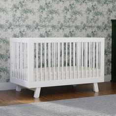 a white crib sitting in front of a wall with green flowers on the walls