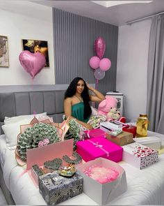 a woman sitting on top of a bed surrounded by boxes and balloons in the shape of hearts