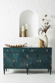 a green dresser with gold accents and vases on the top, in front of a white wall