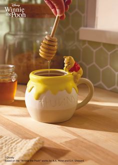 a person pouring honey into a mug with a winnie the pooh figure on it