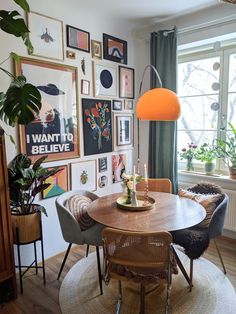 a dining room table with chairs and pictures on the wall behind it, surrounded by potted plants