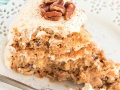 a piece of cake on a white plate with a fork next to it and some pecans in the background