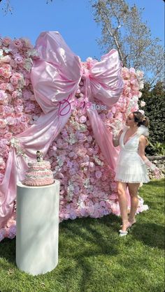 a woman standing in front of a flower covered wall with pink bows on it's head