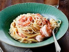 a plate of pasta with shrimp and parmesan cheese on the side next to a glass of water