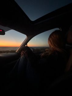 a woman sitting in the driver's seat of a car looking out at the sunset