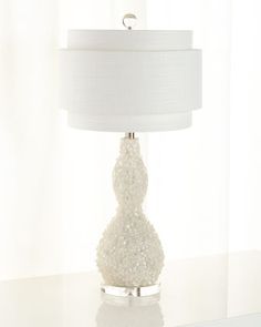 a white lamp sitting on top of a table next to a window with curtains behind it