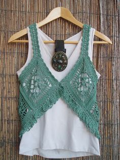 a white shirt with green crochet on it and a button in the middle