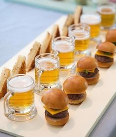 there are many small sandwiches and glasses of beer on the long serving tray with bread