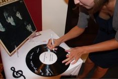 a woman holding a record in front of a white table with black vinyl on it