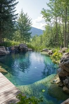 an outdoor swimming pool surrounded by rocks and water features a wooden deck that leads to a small waterfall