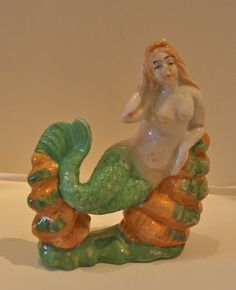 a ceramic figurine of a mermaid sitting on top of a green and orange shell