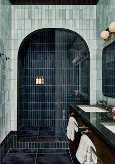 a bathroom with two sinks and blue tiles on the walls, along with an arched shower door