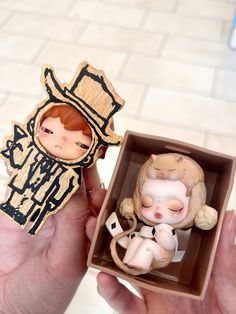 a person is holding a small figurine in a box with another doll inside