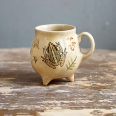 a ceramic cup with a frog painted on it's side sitting on a table