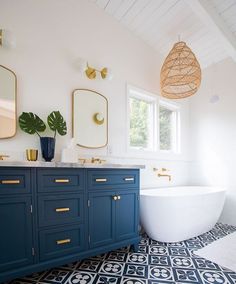 a white bath tub sitting next to a blue cabinet in a bathroom under a window