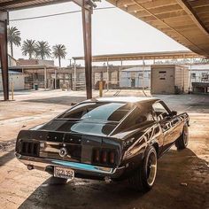 an old mustang sits parked in the middle of a parking lot next to a gas station