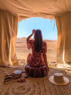 a woman sitting on the ground in front of a tent looking out into the desert