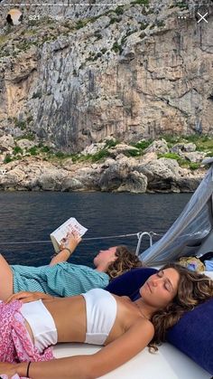 two women lounging on the back of a boat in front of a rocky cliff