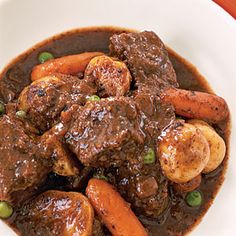 a bowl filled with beef and carrots on top of a white table next to green peas