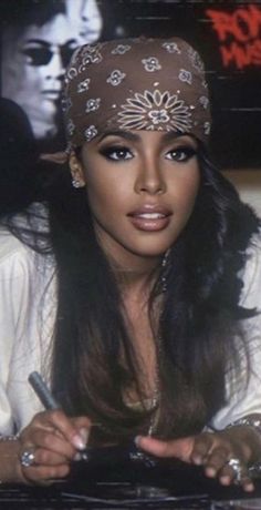 a woman sitting at a table with a pen and paper in her hand while wearing a bandana