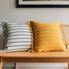 two yellow and black pillows sitting on top of a wooden bench next to a framed photo