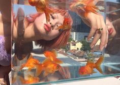 a woman with red hair is looking at goldfish in a fish tank while holding her head