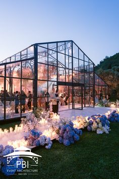 a group of people standing in front of a large glass building with flowers around it