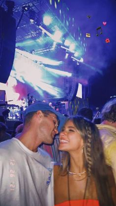 a man and woman standing next to each other at a music festival with bright lights in the background