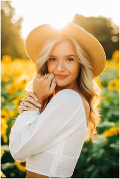 a woman wearing a hat and white shirt posing for a photo in front of sunflowers