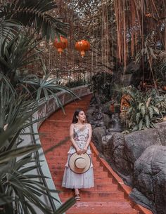 a woman in a dress is sitting on some steps with a hat and palm trees