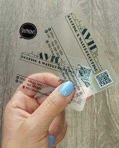 a person holding up two tickets on top of a wooden table with blue nail polish